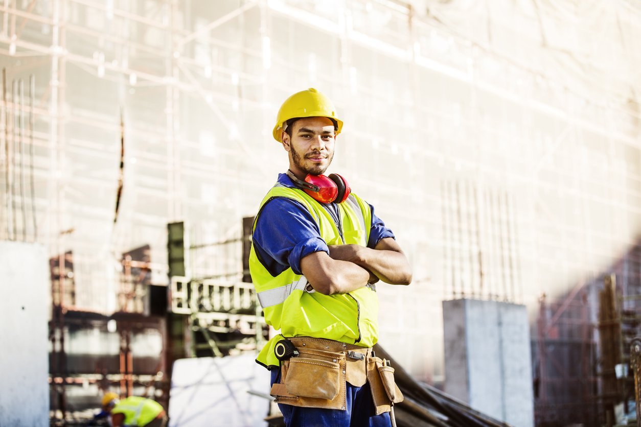 Confident construction worker standing at site with arms folded