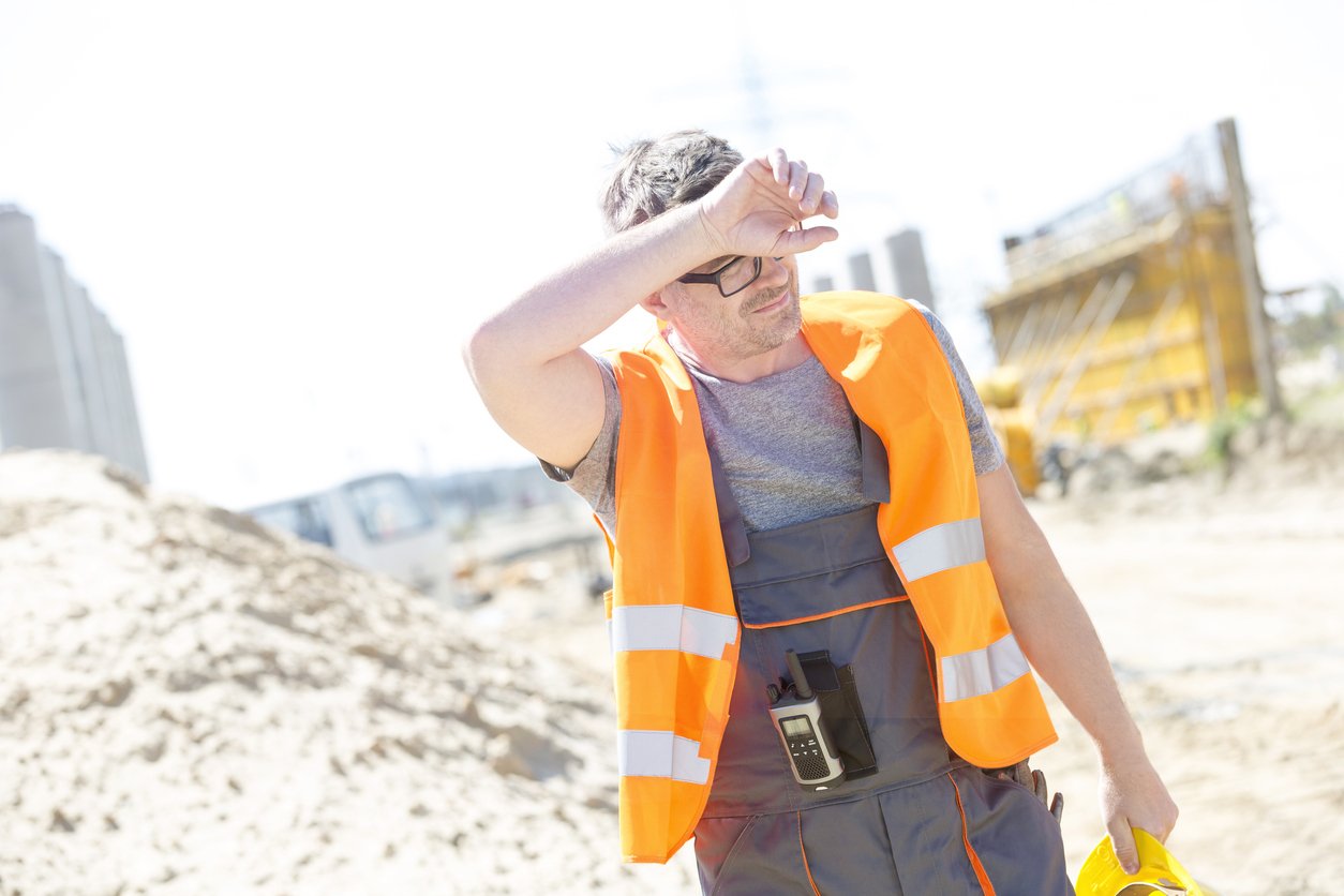 Tired construction worker wiping forehead at site in hot weather
