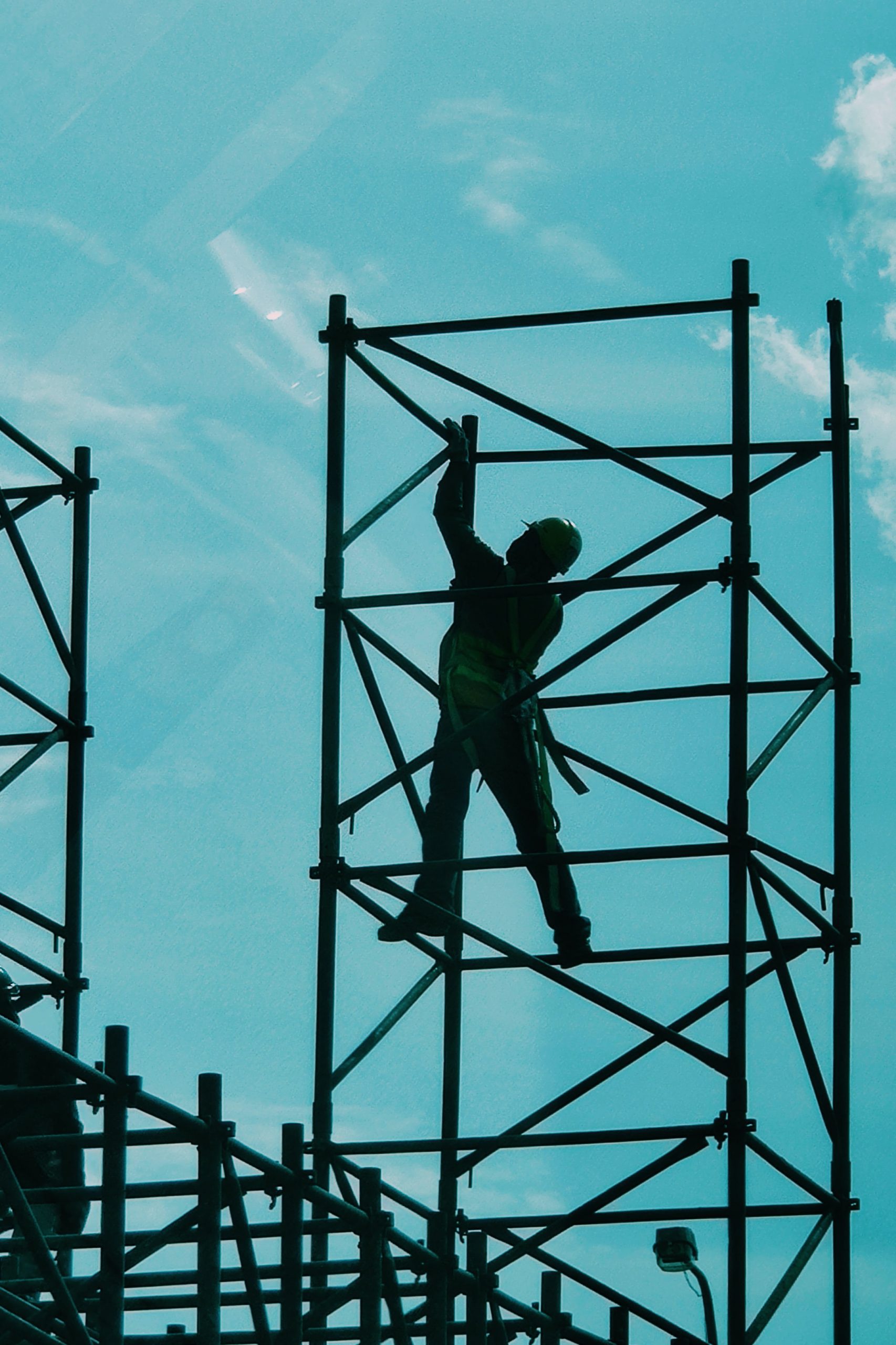 silhouette of man in hardhat on scaffolding against blue sky