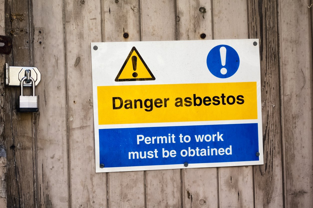 A sign fastened to a gate outside a derelict building warning of the presence of asbestos.
