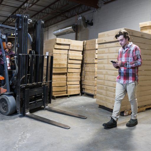 An accident waiting to happen. An industrial worker using a cell phone in a warehouse.